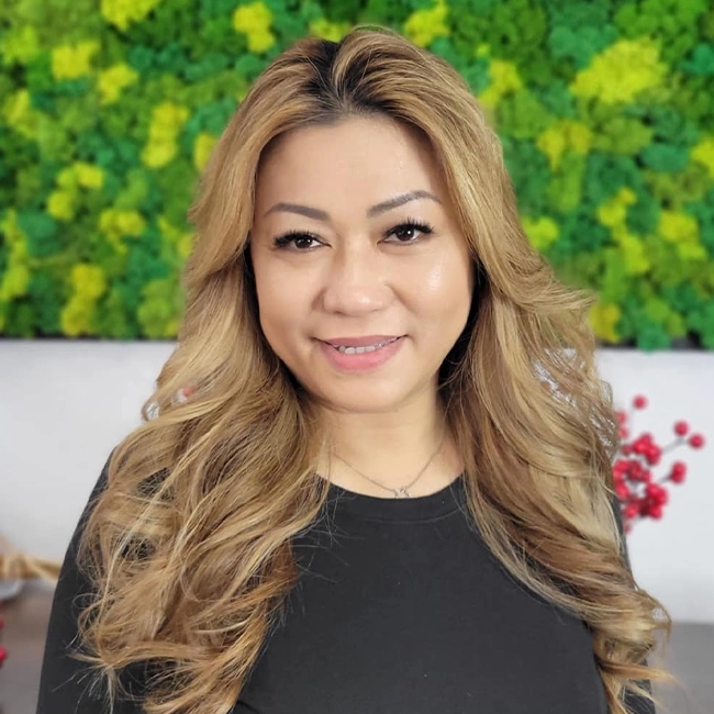 A headshot of Vivian smiling in front of the EDEN Day Spa green moss background board
