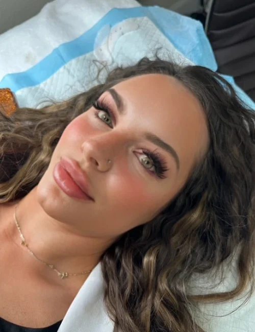 Woman laying flat on her back looking into camera with new lash extensions