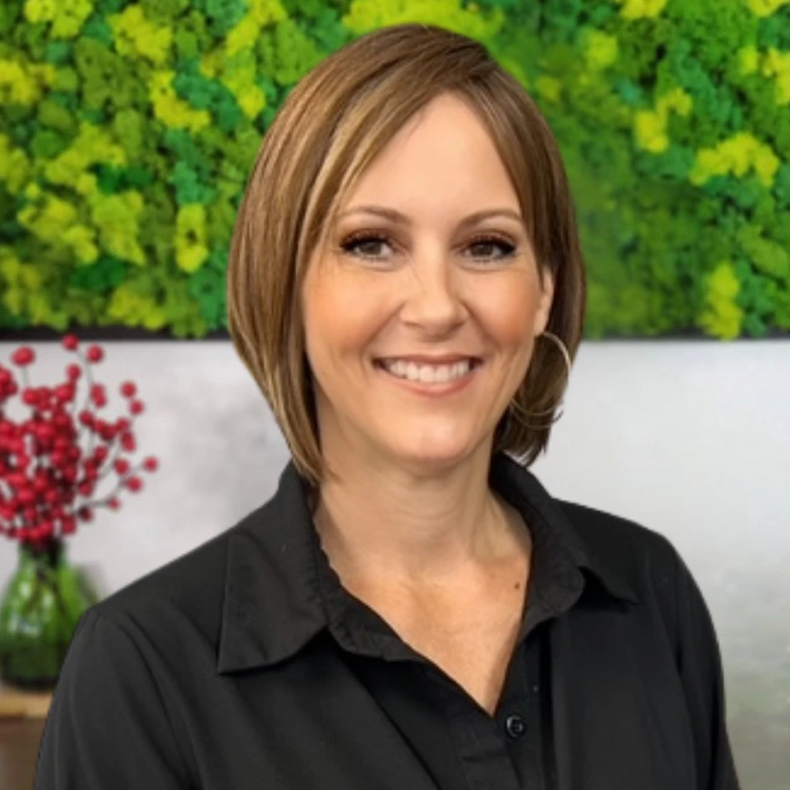 A headshot of Jen smiling in front of the EDEN Day Spa green moss background board