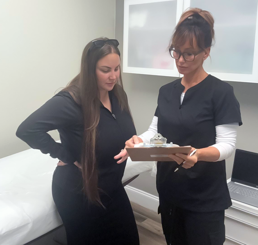 Mindy Jackson showing a client her clipboard in a consult with a patient in the EDEN Aesthetics room